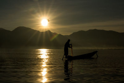 Silhouette man in boat on lake against sky during sunset