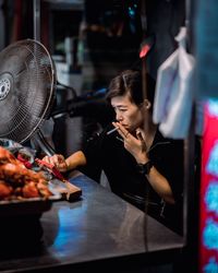 Woman smoking cigarette while using phone by food on table