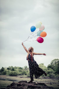 Rear view of woman with balloons in mid-air against sky