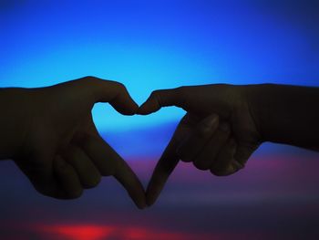 Cropped hands of lesbian couple making heart shape against sky