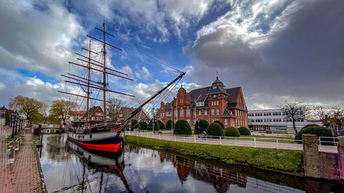 Sailboats moored on canal by buildings against sky