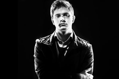 Portrait of young man standing against black background