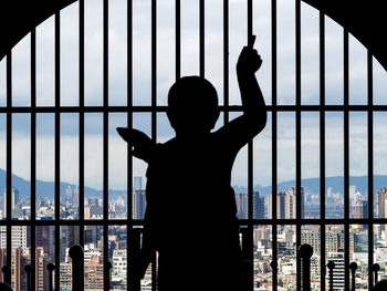 Rear view of silhouette man standing by railing against window