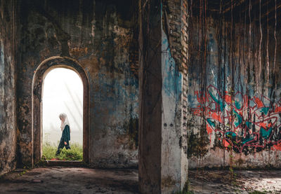 Rear view of woman standing by wall of building