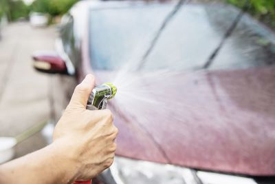 Cropped hand of man spraying water on car