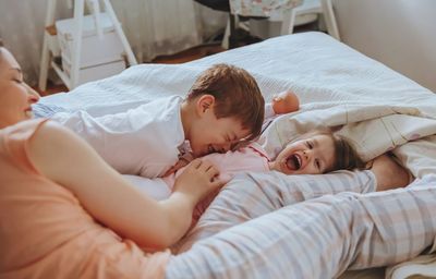 Cheerful mother playing with son and daughter while lying on bed at home