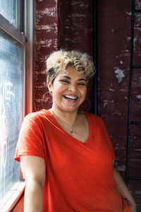 Portrait of cheerful woman with short hair standing by window at home