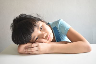 Close-up of girl lying down on table against wall