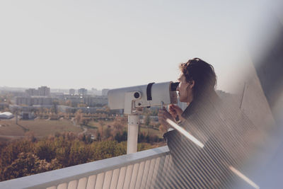 Side view of woman looking through coin-operated binoculars while standing on observation point