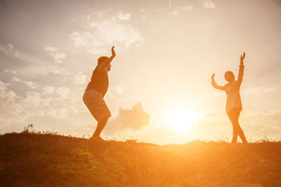 Low angle view of friends standing on field against sky during sunset