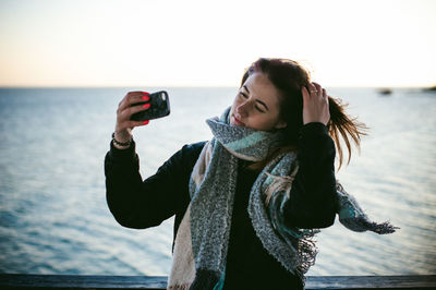 Young woman taking selfie on pier over sea