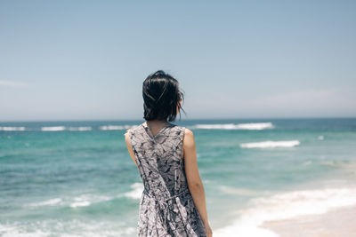 Rear view of woman standing at beach against sky