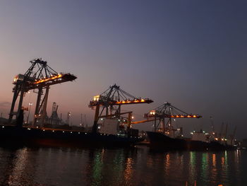 Cranes at commercial dock against clear sky at night