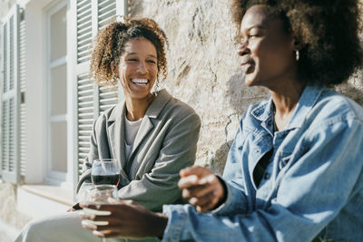 Happy young woman sitting with female friend in backyard on sunny day