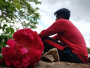 Rear view of man sitting on red flowering plant against sky