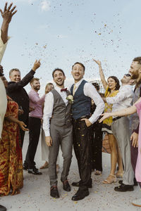 Happy gay couple having fun with guests during wedding ceremony on rooftop