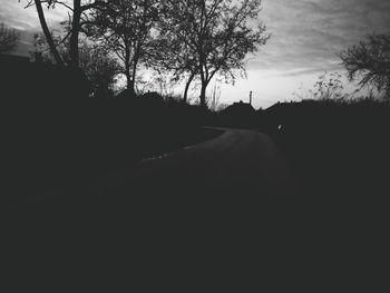 Road amidst silhouette trees against sky