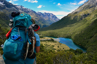 Rear view of young man with backpack standing on mountain against sky