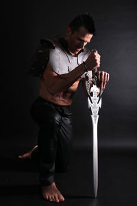 Warrior holding sword kneeling against black background