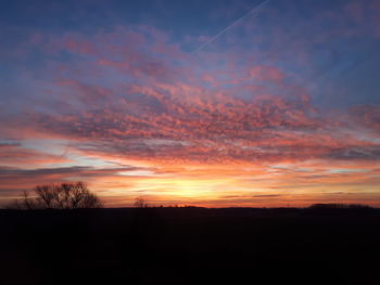 Scenic view of dramatic sky over silhouette trees during sunset