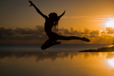 Silhouette woman jumping at sea against sky during sunset