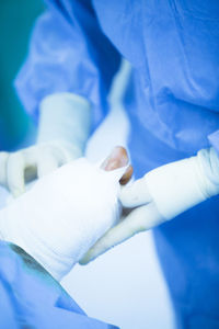 Midsection of surgeon wrapping bandage on patient wound in operating room