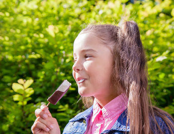 Close-up of smiling girl eating popsicle against plants