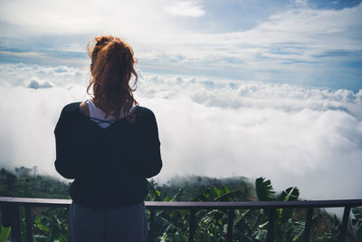 Rear view of woman standing by railing against sky