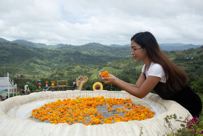 Side view of young woman with orange flower against plants