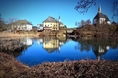 Reflection of buildings on lake against blue sky