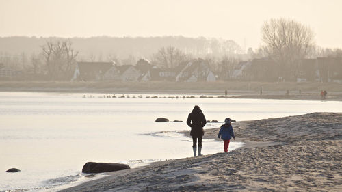 Rear view of children standing on beach against clear sky