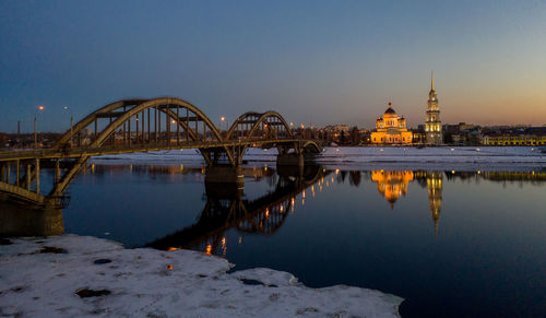 Bridge over river against buildings at dusk