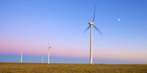 Wind turbines in field against blue sky during dusk