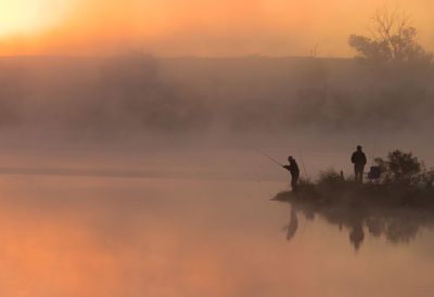 Silhouette people fishing in lake against sky during sunset