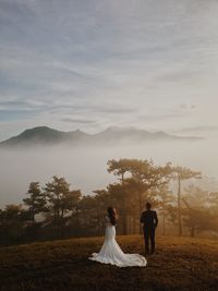 Couple standing on field by mountain against sky