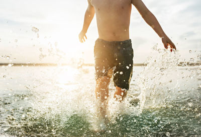Midsection of shirtless boy walking in sea at beach during sunny day