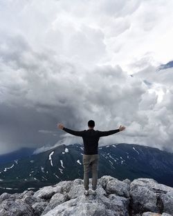 Rear view of man with arms outstretched standing on mountain against cloudy sky