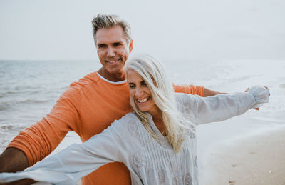 Happy couple with arms outstretched standing at beach