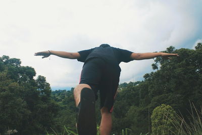 Rear view of man with arms raised against sky