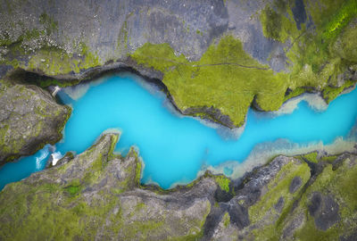 Top view of blue still lake flowing between steep stony coasts covered with green moss in wild nature of iceland