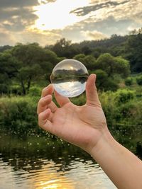 Cropped image of person holding glass against lake