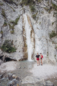 Friends standing by waterfall against rocky mountain