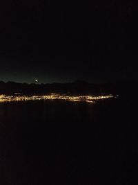 Illuminated city by sea against clear sky at night