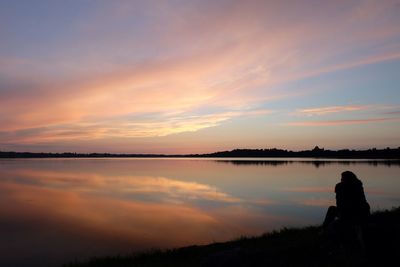 Silhouette woman standing by lake against sky during sunset