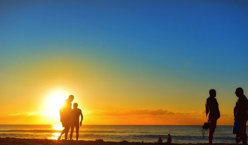 Silhouette people at beach against bright sky during sunset