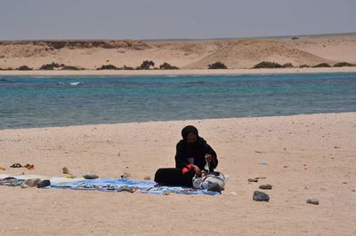 Man sitting on beach against sky