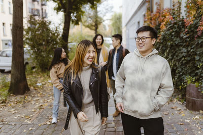 Male and female friends enjoying together while walking on sidewalk