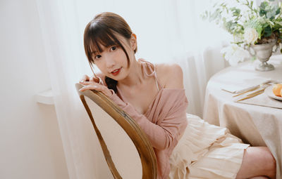 Portrait of young woman using mobile phone while sitting on bed at home
