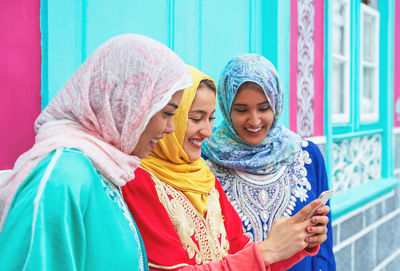 Smiling friends using mobile phone against blue wall
