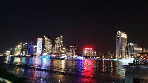 Illuminated buildings by river against sky at night